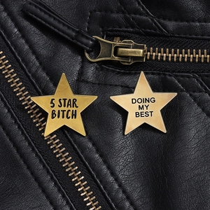 Close-up of golden star pins with slogans pinned on a black leather motorcycle jacket