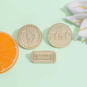 Three elegant gold metal pins including a religious coin and a cinema ticket design
