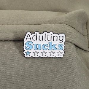 Detailed view of 'Adulting Sucks' enamel pin with stars on green canvas fabric
