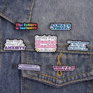 Set of funny mental health enamel pins on denim jacket featuring anxiety and tired themes