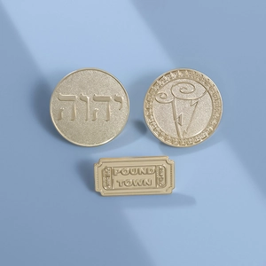 Three-piece gold metal pin set with round engraved motifs and rectangular ticket badge