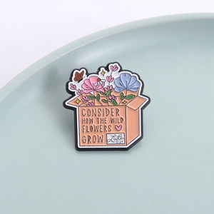 Enamel pin featuring wildflowers in a box with Bible quote Luke 12:27 on a ceramic tray