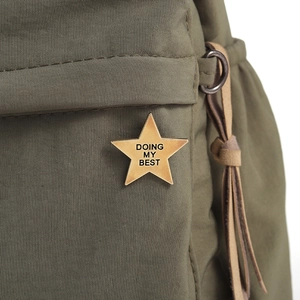 Close-up of a gold star brooch with 'DOING MY BEST' engraving on green nylon fabric