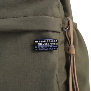 Close-up of enamel humor badge with sarcastic text pinned to a green canvas backpack