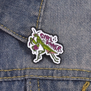 Pin's émaillé mante religieuse avec texte Girl Dinner sur une veste en denim