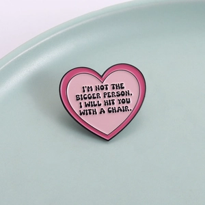 Pink heart-shaped enamel pin with humorous black lettering on a clean background