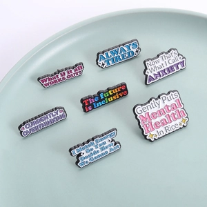 Set of 7 colorful enamel pins with mental health slogans in a blue ceramic dish