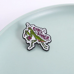 Quirky green mantis enamel pin with Girl Dinner text on a ceramic plate background