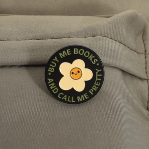 Detail of round enamel pin with floral design and text Buy Me Books and Call Me Pretty