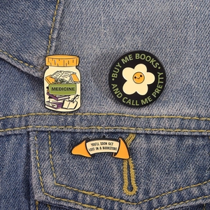 Detailed view of three literary enamel pins pinned on blue denim fabric