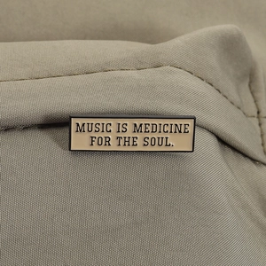 Detail view of Music Is Medicine For The Soul quote enamel pin on canvas fabric