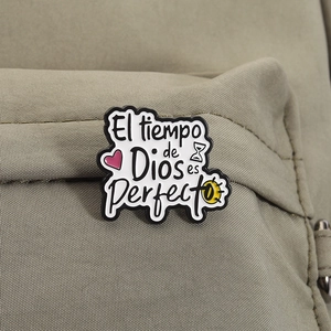 Macro detail of enamel pin with Spanish text El tiempo de Dios es Perfecto on green fabric