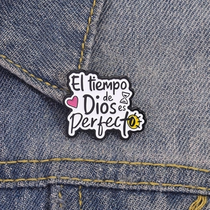 Detailed enamel pin on denim showing El tiempo de Dios es Perfecto text with icons