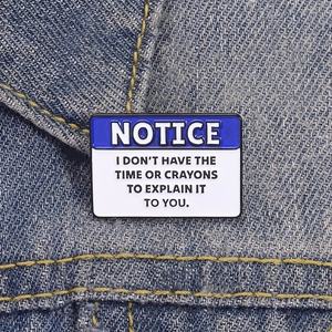 Funny blue and white notice enamel pin with ironic slogan on denim jacket fabric