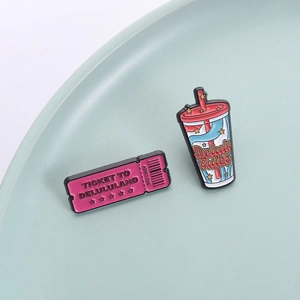Emaille-Pins-Set mit rosa Ticket und Delulu Juice Motiv auf einem eleganten Keramikteller