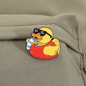Gros plan d'un pin's en émail canard jaune avec lunettes sur un tissu en toile olive