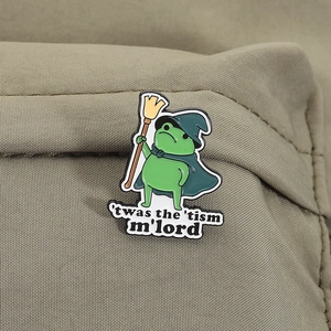 Macro shot of green enamel frog wizard pin with broom on olive canvas texture background