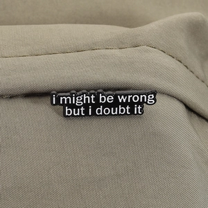 Close-up of enamel pin with quote 'i might be wrong but i doubt it' on canvas