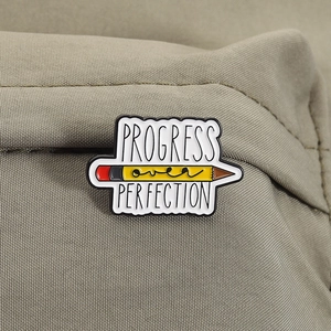 Détail du pin's émaillé crayon avec devise 'Progress Over Perfection' sur sac