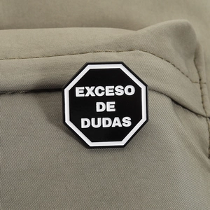 Détail d'un pin's octogonal en émail avec le texte Exceso de Dudas sur tissu
