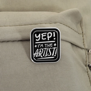 Close-up of black enamel artist badge with white slogan on a canvas backpack strap