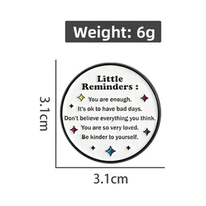 Detail view of 3.1cm round enamel pin with Little Reminders quote on white background