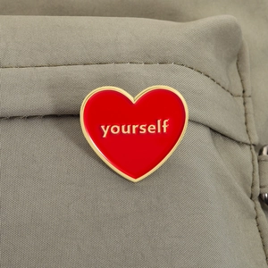 Detailed view of red heart enamel pin with yourself lettering on khaki fabric background