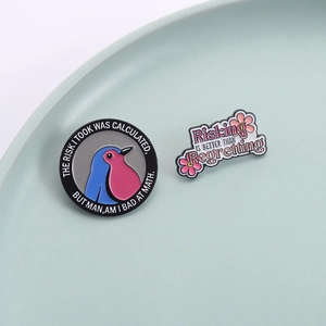 Enamel pins with bird and flower designs featuring motivational quotes on a ceramic tray