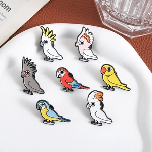 Set of seven colorful enamel parrot brooches featuring various cute bird species on a plate