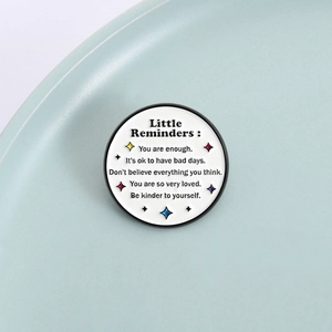 Round enamel pin with Little Reminders quote and colorful stars on a white background