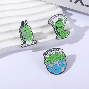 Lot de trois broches en émail en forme de pois avec jeux de mots sur support blanc ondulé