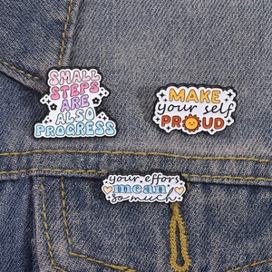 Set of three inspirational cartoon enamel pins on blue denim fabric background