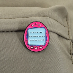 Dettaglio della spilla in smalto rosa stile pet virtuale con testo spagnolo su tessuto