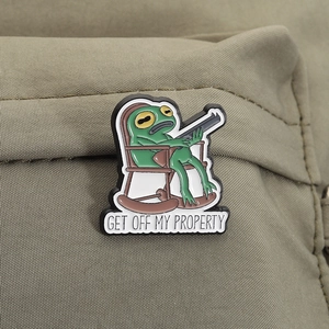 Detailaufnahme der lustigen Frosch-Emaille-Anstecknadel mit Spruch auf olivgrünem Rucksack