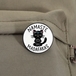 Funny black cat namaste enamel pin detail shown on an olive green canvas bag
