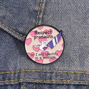 Funny cat heart enamel pin with Respect Pronouns quote on blue denim jacket