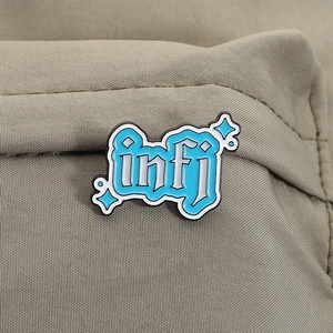 Gros plan sur le pin's émaillé INFJ bleu ciel épinglé sur un tissu kaki texturé