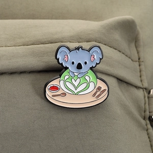Detail of cute koala enamel pin on a green fabric backpack featuring a meal on a plate