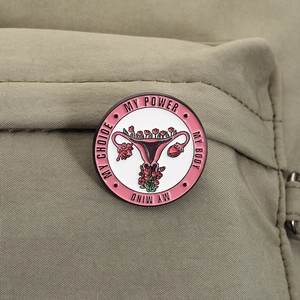 Close-up of a pink uterus power enamel pin attached to a green canvas backpack
