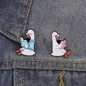 Detail of cartoon white duck enamel pins with glasses reading books on denim jacket
