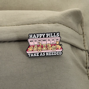 Macro detail of Happy Pills enamel pin with cute puppies on khaki textured fabric