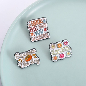 Three creative enamel pins with inspirational quotes on a soft mint ceramic tray