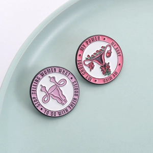 Feminist enamel pins with flower womb designs and empowering quotes on a ceramic plate