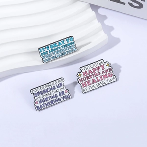Tre spille smaltate curative in blu, rosa e viola su un espositore bianco ondulato