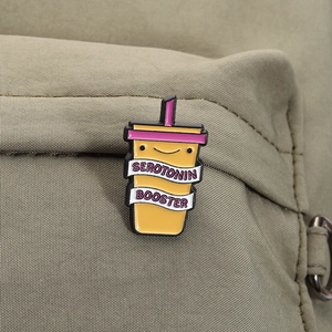Detail of yellow serotonin booster enamel pin on a green canvas backpack strap