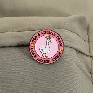 Detail of God's Silliest Goose enamel pin on canvas with pink cartoon duck and gold halo