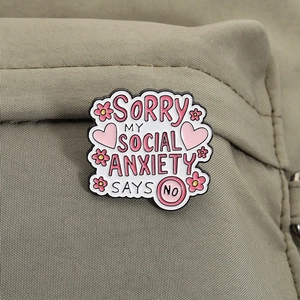 Close-up of pink enamel pin with social anxiety slogan and flowers on khaki fabric