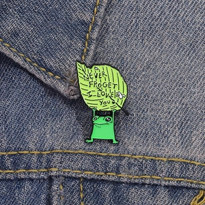 Spilla divertente a forma di rana verde con testo su risvolto di giacca di jeans blu