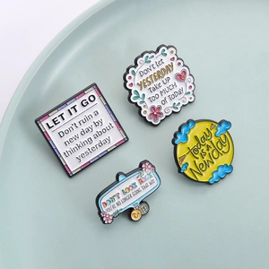 Lot de quatre pins émaillés colorés avec citations motivantes sur une assiette bleu clair