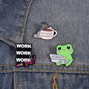 Creative office humor enamel pins featuring cat coffee and frog laptop on denim background